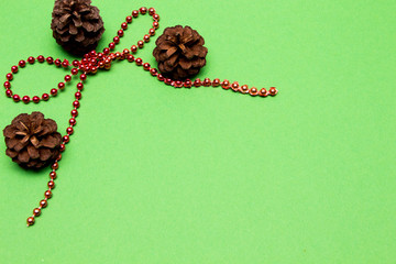 Christmas decoration. Bow and red beads and fir-cone and snowflake on green background.