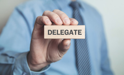 Businessman showing Delegate word in wooden block. Business concept