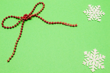 Holiday decoration. Bow, red beads and snowflake on green background.