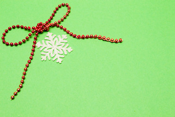 Holiday decoration. Bow, red beads and snowflake on green background.