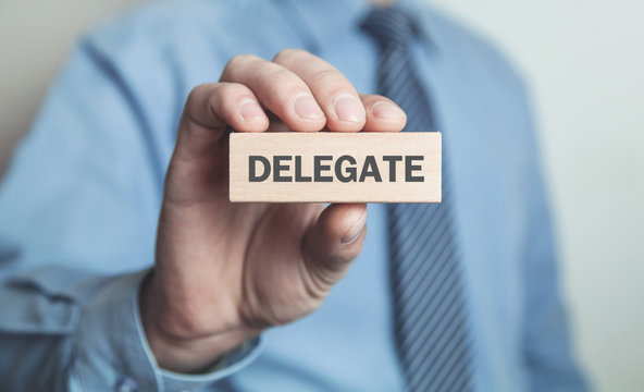 Businessman showing Delegate word in wooden block. Business concept