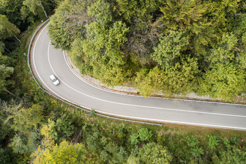Mountain road in the woods with passing car. Aerial view.