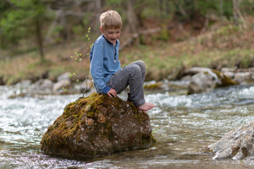 Boy sitting on rock in creek