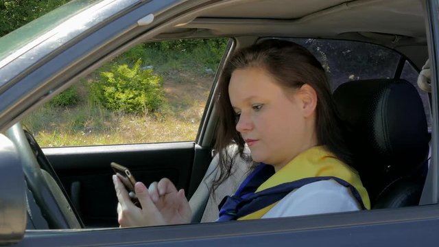 woman sits behind the wheel of a car and uses a smartphone