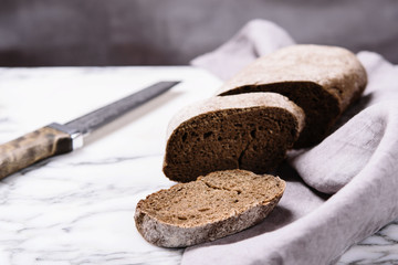 Freshly baked sliced rye bread and knife on linen napkin on marble table. Selective focus