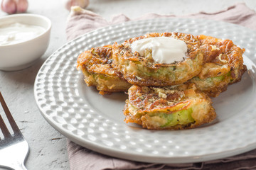 Fried zucchini slices in egg batter with garlic on a plate.