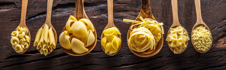 Verschillende soorten pasta in houten lepels op tafel. Bovenaanzicht.