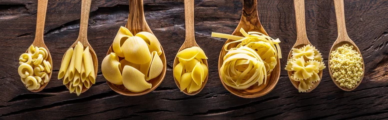 Foto op Plexiglas Eetkamer Verschillende soorten pasta in houten lepels op tafel. Bovenaanzicht.