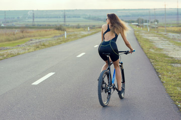 A girl riding a mountain bike on an asphalt road, beautiful portrait of a cyclist at sunset	