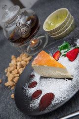 Dessert Cheesecake on a black plate stands on a wooden table tea kettle with a candle and cane sugar. Чизкейк на черной тарелке стоит на деревянном столе чайник чая свеча и тростниковый сахар.
