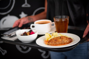 The girl holds a tray in the dining room, on a salad tray, a hot dish, compote, soup. Девушка держит поднос в столовой, на подносе салат, горячее блюдо, компот, суп.