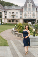 Pregnant woman in dress holds hands on belly