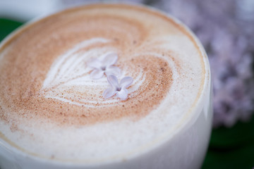 Macro photography of a cappuccino cup on the foam lie the flowers of the lilac....