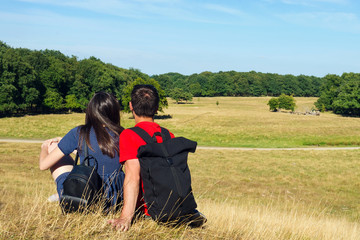 Naklejka na ściany i meble Young couple are sitting on the grass and looking at a beautiful landscape. Concept travel. Summer.