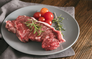 raw steak with rosemary and tomatoes on a gray plate on rustic wood