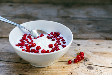 natural yoghurt cream with fresh red currants in a white bowl, healthy breakfast or dessert on a rustic wooden table, copy space
