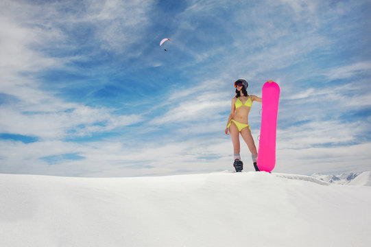Young sexy girl in the yellow swimsuit with a snowboard standing on the snow cover