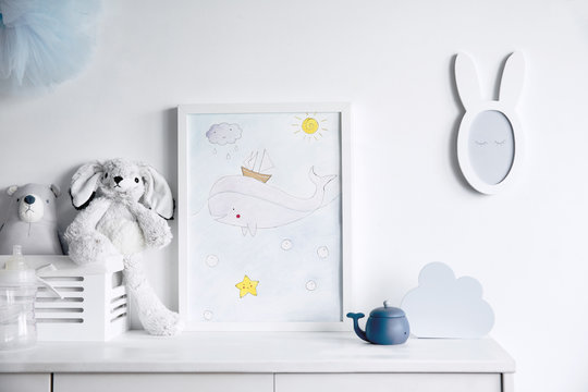 Stylish scandinavian newborn baby room with toys, rabbit, small mirror and cloud. Modern interior with mock up photo frame.