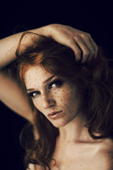 Beautiful young woman with red hair and freckles portrait, beauty shoot on dark background, mysterious dark mood