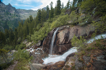 Fototapeta na wymiar Великолепный горный пейзаж с водопадом. Красивый горный ручей и волшебные горные цветы