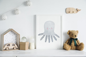 Stylish scandinavian nursery shelf with mock up photo frame, bottle with milk, teddy bears and wooden toys. Modern interior with white walls and wooden accessories..