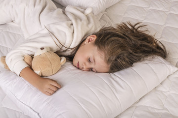 Cute girl sleeping and hugging her teddy bear in the bed