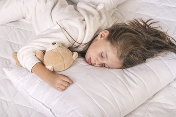 Cute girl sleeping and hugging her teddy bear in the bed