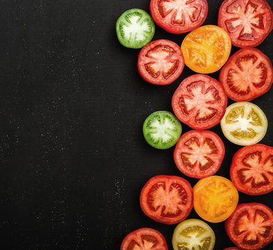Tomatoes of different colors cut in half. Fresh and juicy vegetables on black stone background, top view