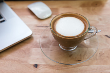 Cappuccino coffee cup with laptop computer and mouse on wooden table