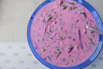 Cold beet soup with herbs on the table.On a table with a light cloth there is a blue plate with cold vegetable soup,