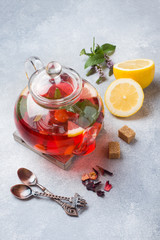 Glass teapot with tea, mint and lemon on grey table with copy space