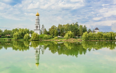 The white bell tower stands on the shore of the lake and is reflected in the water