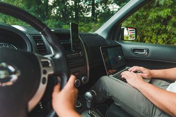 couple in car. man working on laptop in road trip