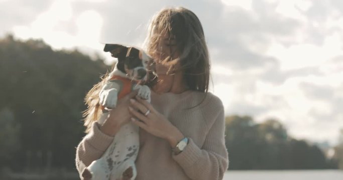 Portrait of beautiful young woman playing with dog jack russell terrier on the lake shore. A girl whirl in dance with a cute puppy. 4K video shooting