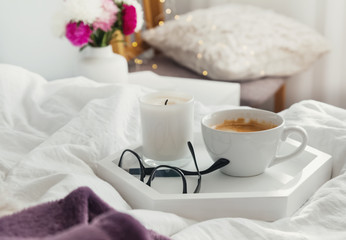 Fototapeta na wymiar Coffee, candle and glasses on the tray standing on the bed.