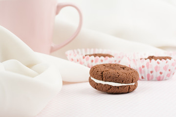 Chocolate cookie in the form of a sandwich with cream on pastel pink background. Close up, copy space.