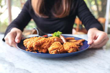 Closeup image of a woman holding a plate of fried chicken and french fries in restaurant