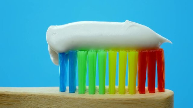 Toothpaste squeezed from tube into rainbow wooden brush for tooth cleaning isolated on blue background