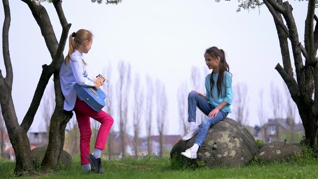 two little girl rehearsing a song outdoor play jeans guitar. beautiful view in the background in the countryside