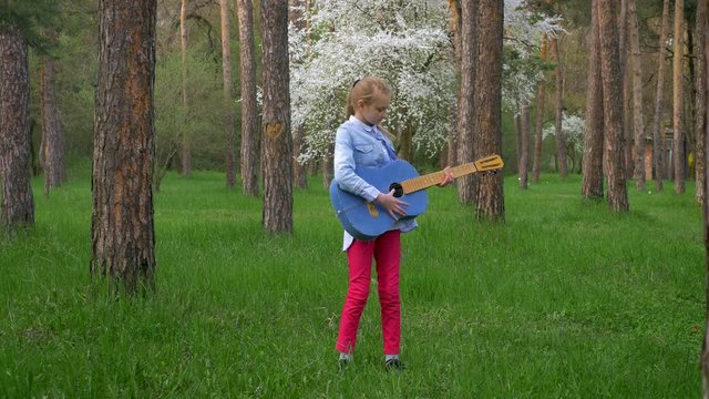 Attractive little girl standing in spring Park,blonde plays guitar music