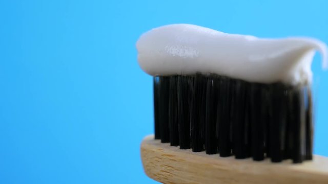 Toothpaste squeezed from tube into black wooden brush for tooth cleaning isolated on blue background