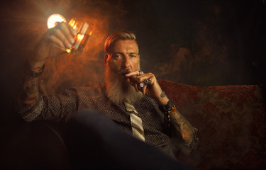 Portrait eines attraktiven Geschäftsmannes mit einer Zigarre und einem Glas Whiskey vor dunklem...