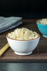 A bowl of cooked white rice on a table with dark copy space background