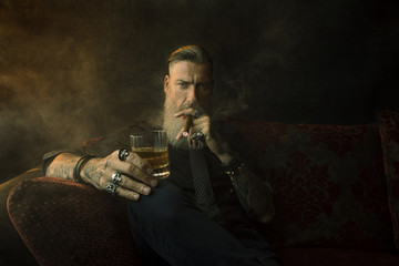 Portrait eines attraktiven Geschäftsmannes mit einer Zigarre und einem Glas Whiskey vor dunklem...