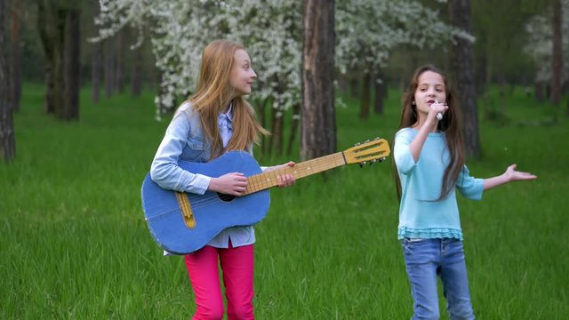 imitation pop musician performance in the forest Park Happy little girlfriends fool around dancing and sing songs playing guitar.shaking long her hair head. springtime