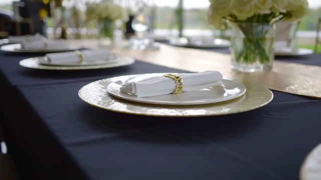close-up moving shot of white plates and wrapped napkins on a table with dark blue covering in a restaurant