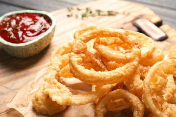 Homemade crunchy fried onion rings and sauce on cutting board, closeup