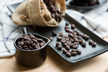 Cup full of coffee beans, sackcloth and on black plate
