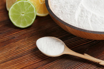 Spoon and bowl with baking soda on wooden table, closeup