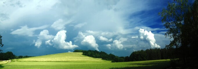Scenic landscape with storm cloud in background over green agriculture fields,trees and meadows at spring daylight, dramatic clouds, sky.Relaxing nature,sunshine.Panoramic photo.Czech Repulic, Europe.